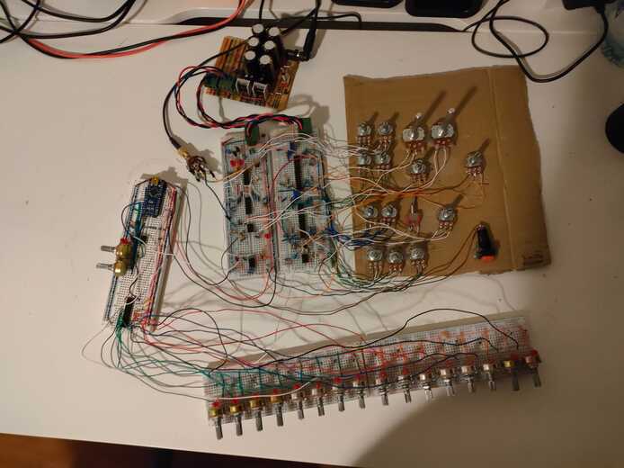 5 breadboards all connected together. The bottom two are populated with 16 knobs in a row while the rest have various circuitry. Many knobs are attached to a cardboard sheet, all wired into the breadboards. The power supply is connected to the breadboards.