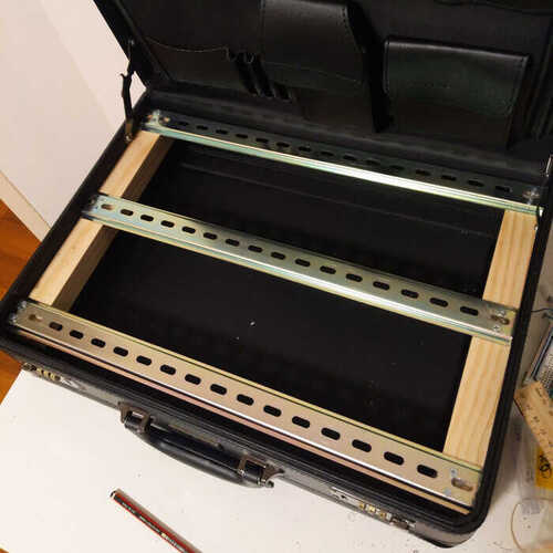 A briefcase with a wooden and metal frame build inside for holding two rows of synth modules