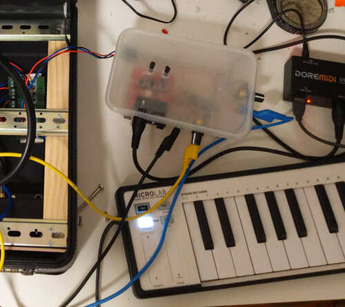 A takeaway container with some cables coming out connecting a MIDI host to the briefcase synth